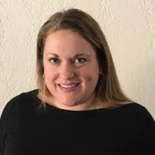 Head-and-shoulders portrait of a person with light brown hair wearing a black top against a light-colored wall.